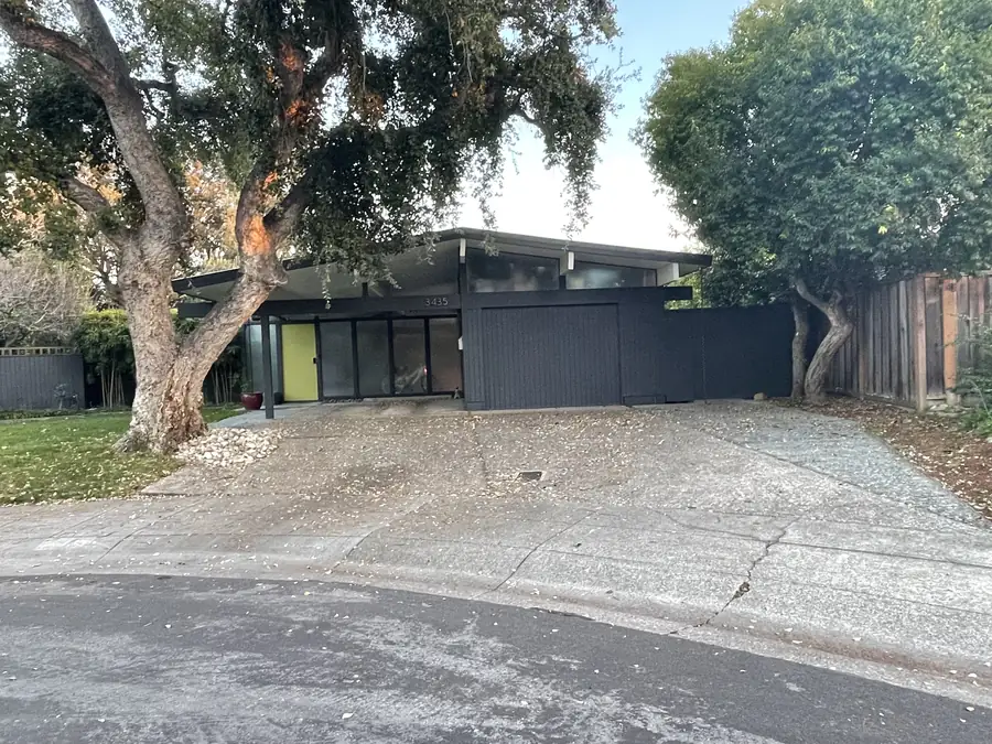 An Eichler elevation under a mature oak, with chartreuse door panels set into dark siding.
