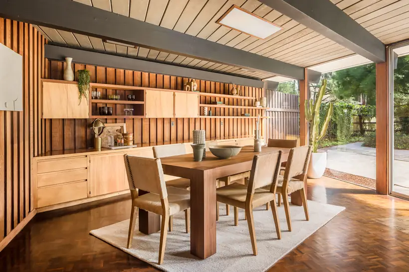 The dining room: original built-in birch casework set against a redwood batten wall, parquet floor and a full glass wall onto the garden.
