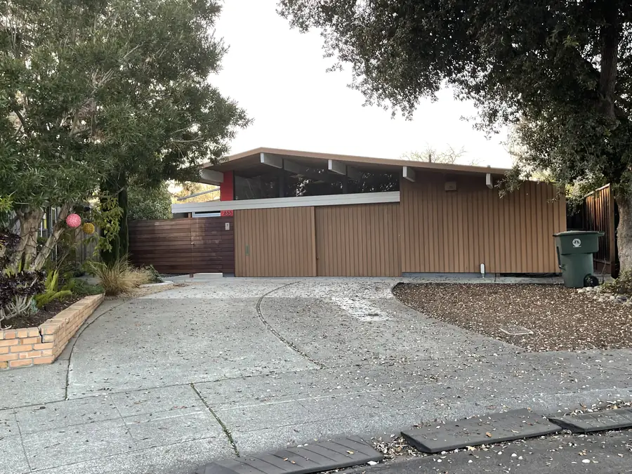 A wood-clad Eichler with deep carport and low-slope roofline at dusk.